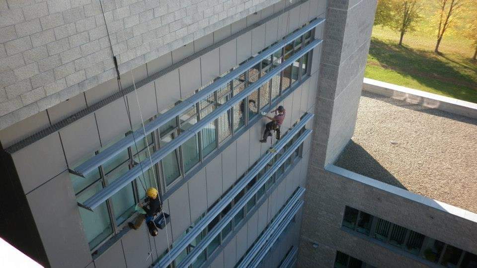 Osoba siedzi na parapecie przy oknie, w tle elewacja budynku z niebieskimi 

balustradami.